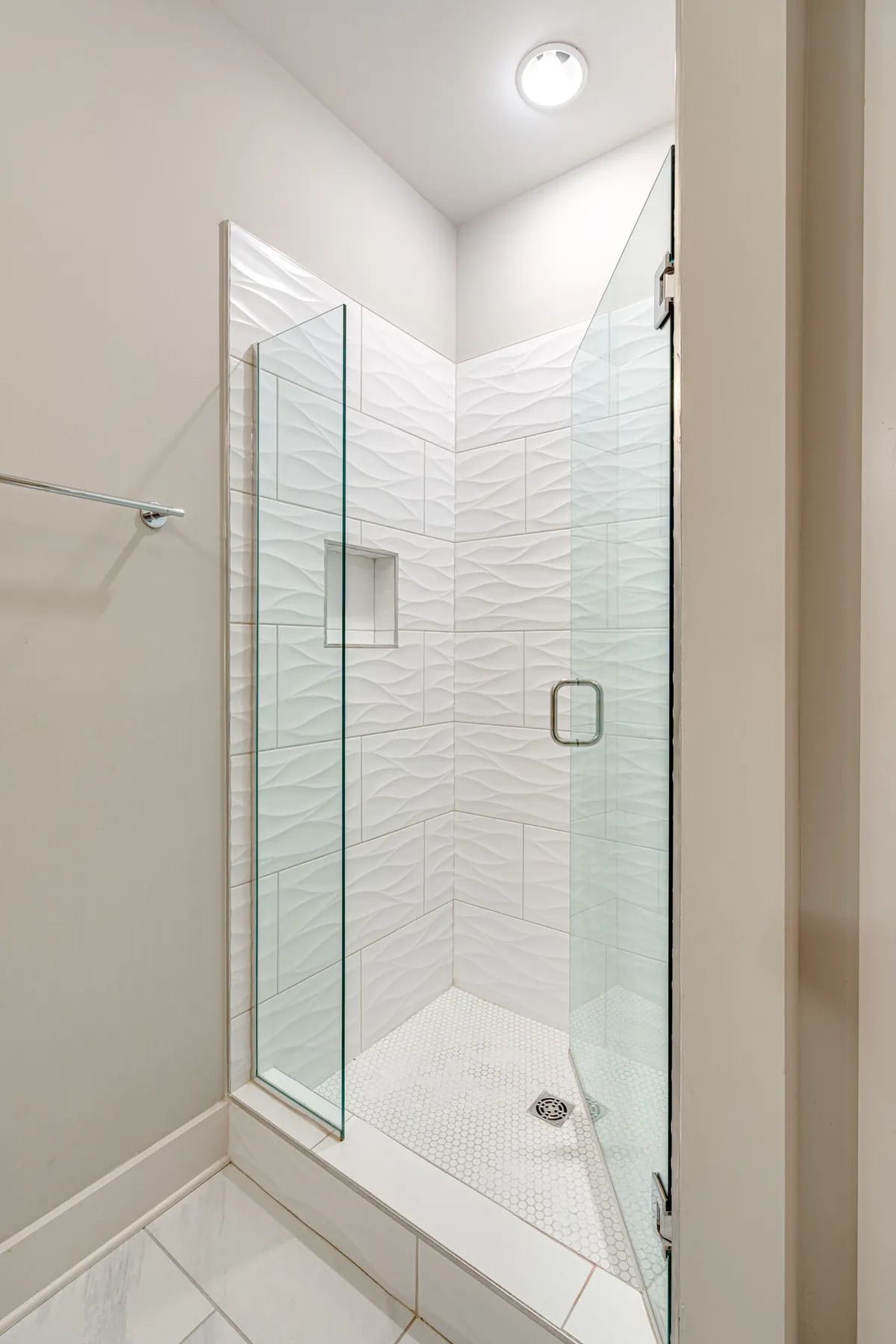 A modern ensuite bathroom featuring a glass shower enclosure, textured wall tiles, and hexagonal floor tiles, exuding a spa-like ambiance. The design is sleek and contemporary, emphasizing relaxation and privacy.