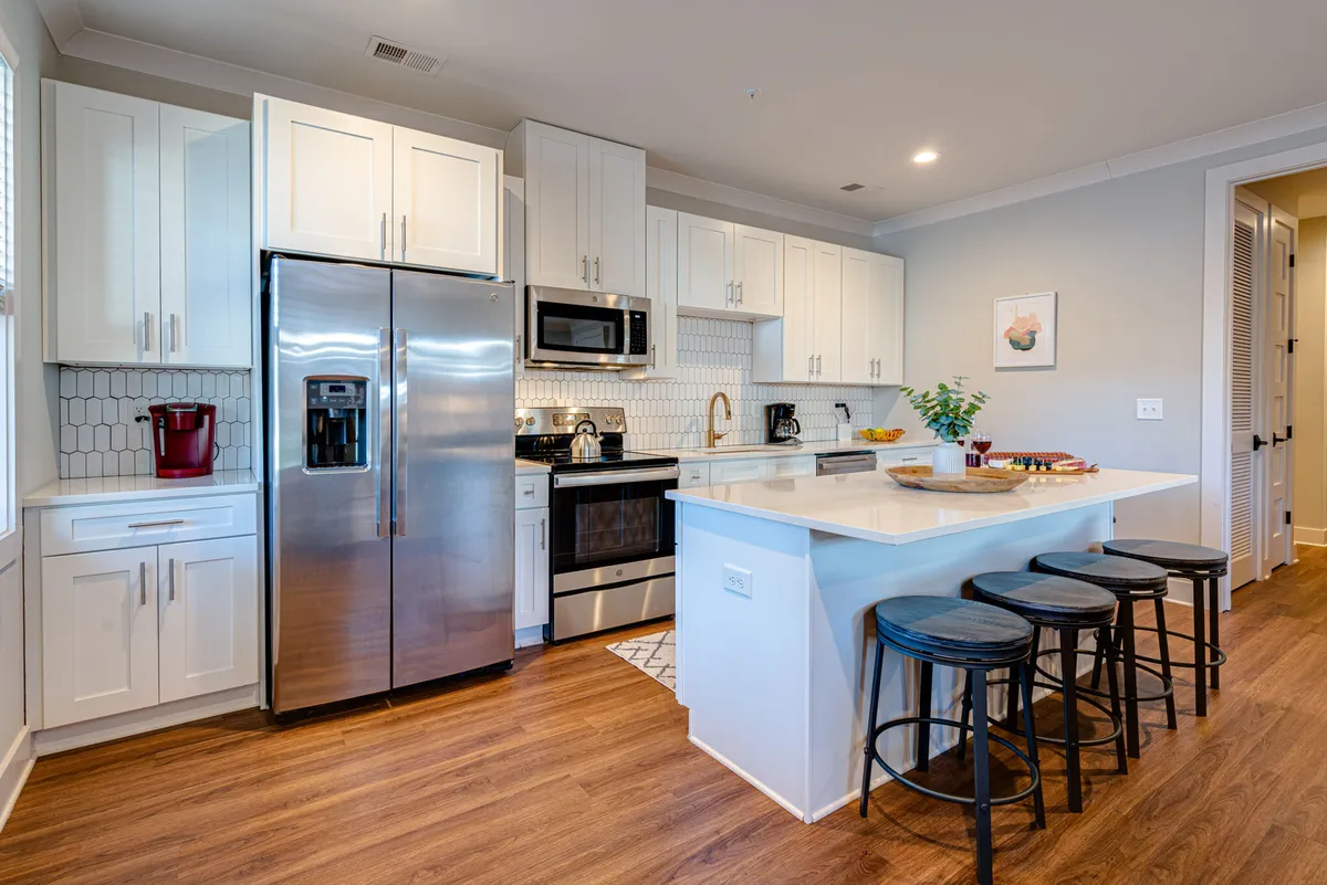 A modern kitchen featuring stainless steel appliances, sleek white cabinetry, a kitchen island with seating, and decorative artwork on the wall. The space is bright, open, and well-equipped, creating an inviting environment for cooking and casual dining.