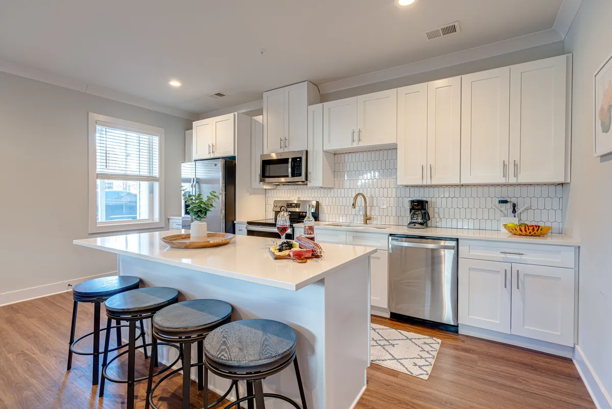 A modern kitchen with a large island countertop, stainless steel appliances, and white cabinetry. The decorative fruit bowl and ample counter space invite guests to cook, bake, or socialize. The kitchen's open layout is perfect for meal prep and casual gatherings.
