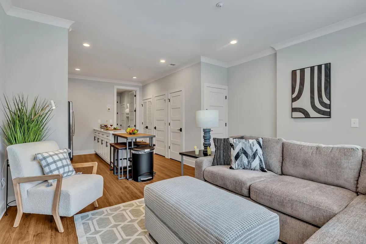 This image features a comfortable sofa and coffee table in the foreground, with a spacious kitchen island and stainless steel appliances visible in the background. Decorative artwork provides a modern touch, and the open-concept design allows for seamless interaction between living and kitchen areas.