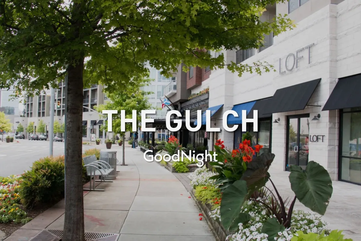 A lively exterior shot of a Nashville street with manicured flower beds, modern storefronts, and benches, where people gather for strolls, shopping, and local events. The welcoming mood and vibrant details invite families to explore the neighborhood.